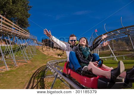 Excited young couple driving alpine coaster while enjoying beautiful sunny day in the nature