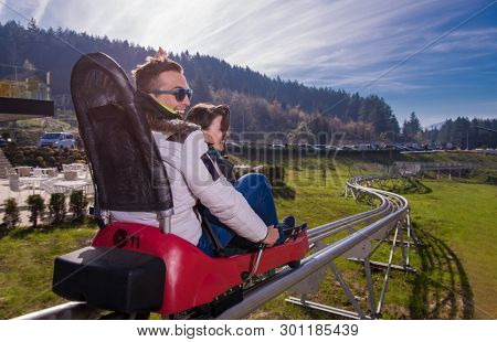 Excited young couple driving alpine coaster while enjoying beautiful sunny day in the nature
