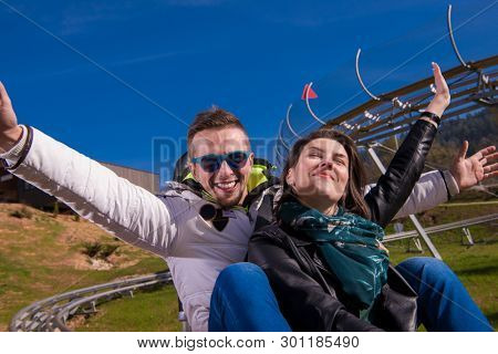 Excited young couple driving alpine coaster while enjoying beautiful sunny day in the nature