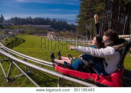 Excited young couple driving alpine coaster while enjoying beautiful sunny day in the nature