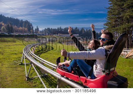 Excited young couple driving alpine coaster while enjoying beautiful sunny day in the nature