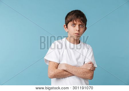 Portrait of serious teen boy 10-12y with freckles wearing white casual t-shirt looking at camera isolated over blue background