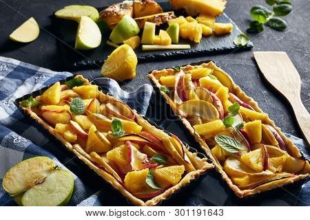 French Pineapple And Apple Sweet Tarts  In Rectangular Tart Pans On A Concrete Table With Kitchen To