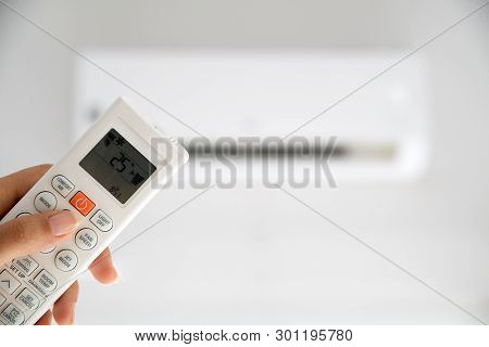 Woman Hand Holding Remote Controller Directed On The Air Conditioner Inside The Room And Set At Ambi