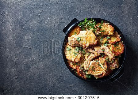 Delicious Browned Pork Chops On Bone And Hash Brown Casserole In A Black Ceramic Pan On A Concrete T