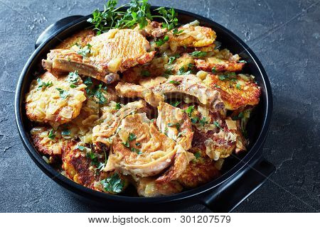 Delicious Browned Pork Chops On Bone And Hash Brown Stew In A Black Ceramic Pan On A Concrete Table,
