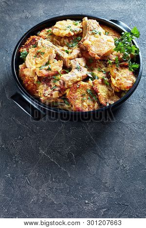 Browned Pork Chops On Bone And Hash Brown Stew In A Black Ceramic Pan On A Concrete Table, Vertical 