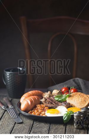 Full English Breakfast With Fried Eggs, Sausages, Bacon, Beans, Toast And Tomatoes On Rustic Wooden 