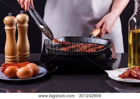 Young Woman In A Gray Apron Fries Bacon