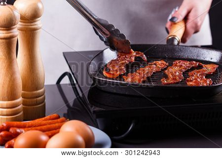 Young Woman In A Gray Apron Fries Bacon