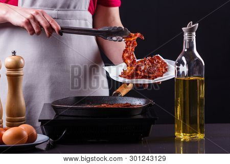 Young Woman In A Gray Apron Fries Bacon