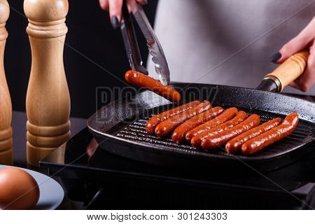 Young Woman In A Gray Apron Fries Sausages