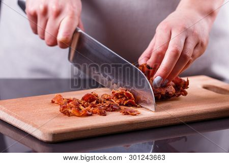 Young Woman In A Gray Apron Cuts Roasted Bacon
