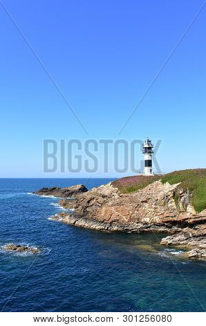 Lighthouse At Isla Pancha. Island With Cliff And Violet Flowers, Ribadeo, Spain, Sunny Day.