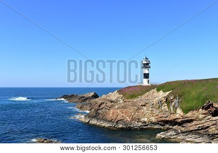 Lighthouse At Isla Pancha. Island With Cliff And Violet Flowers, Ribadeo, Spain, Sunny Day.