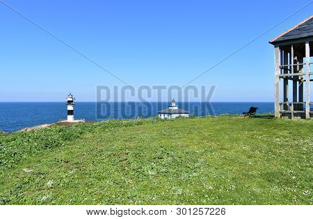 Island With Two Lighthouses From A Viewpoint With Grass, Hut And Bench. Isla Pancha, Ribadeo, Spain,
