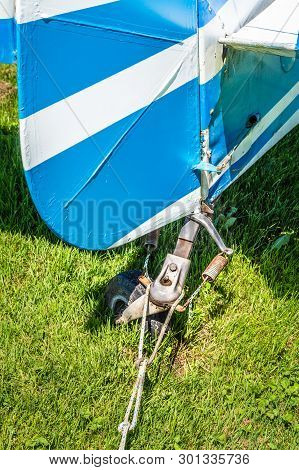 Rear View Of Tail Rudder And Wheel Of A Vintage Aircraft Parked On A Grass Field.