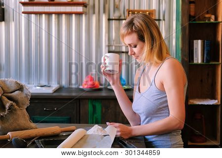 A Beautiful Freckled Blonde Girl In Pajamas Is Standing Near The Kitchen Table, Drinking Fock, Tea A