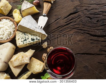 Cheeses with organic cheeses, fruits, nuts and wine on wooden background. Top view. Tasty cheese starter.