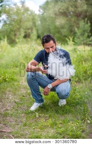 Stylish Brutal Man Vaping An Electronic Cigarette In The Forest. Non-tobacco Smoking.