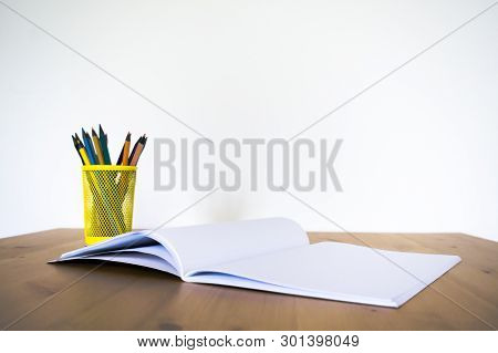 Notebook And Glass With Pencils And Pens On A Wooden Table. Front View