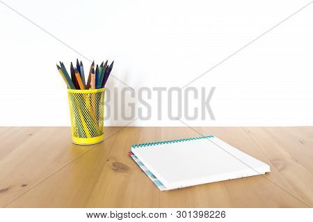 Notebook Sketch Book And Glass With Pencils And Pens On A Wooden Table. Front View
