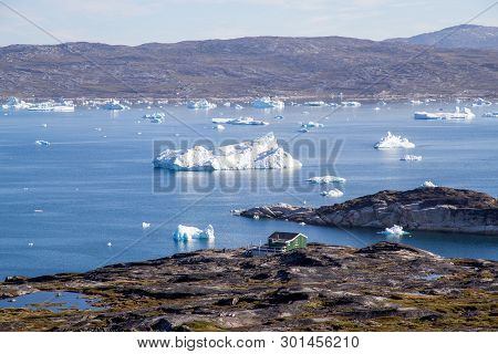 Ilulissat, Greenland - July 08, 2018: A Green Wooden House At The Coast With Icebergs In The Backgro