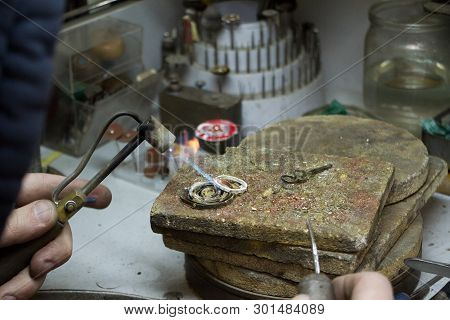The Master Jeweler Holds The Working Tool In His Hands And Makes Jewelery At His Workplace