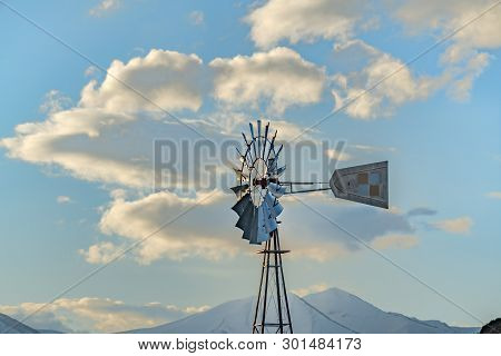 Windpump With A Snow Covered Mountain And Cloudy Blue Sky In The Background