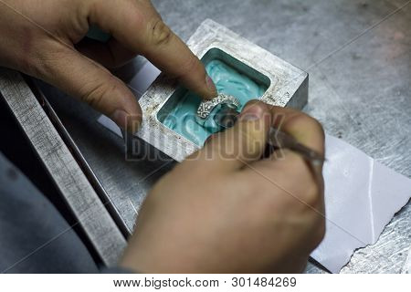 The Master Jeweler Holds The Working Tool In His Hands And Makes Jewelery At His Workplace