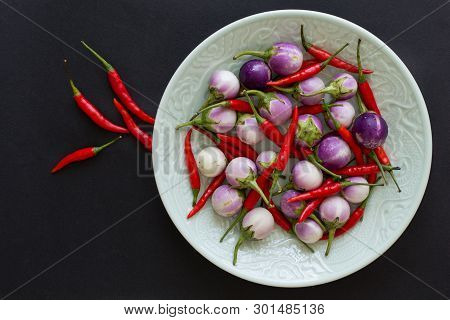 Purple Thai Eggplants And Hot Chili Peppers On A Green Plate And Nearby On A Black Background. Asian
