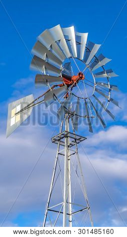 Clear Vertical Shiny Steel Windpump Against A Vibrant Blue Sky With Cottony Clouds