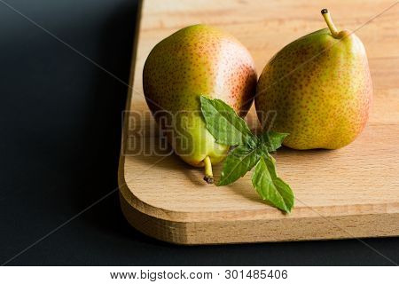 Two Pears With Fresh Basil Leaves On A Wooden Cutting Board With Black Background