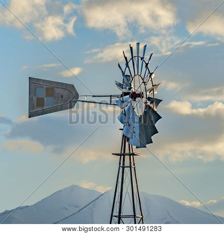 Square Windpump With A Snow Covered Mountain And Cloudy Blue Sky In The Background