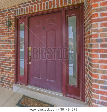 Square Facade Of A Home With A Red Front Door And Reflective Sidelights And Windows