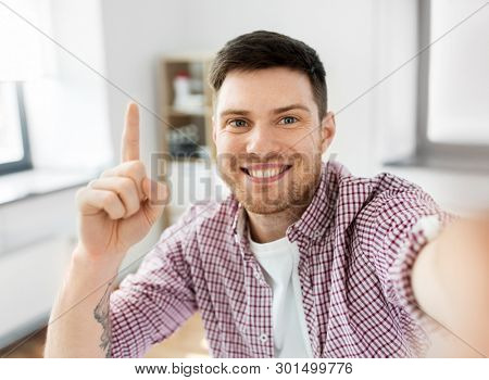 blogging, videoblog and people concept - man or blogger videoblogging or taking selfie and pointing finger up at home