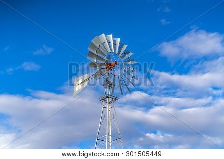 Shiny Steel Windpump Against A Vibrant Blue Sky With Cottony Clouds
