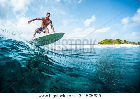 HIMMAFUSHI / MALDIVES - MARCH 10, 2019: Young surfer with lean muscular body rides the tropical wave