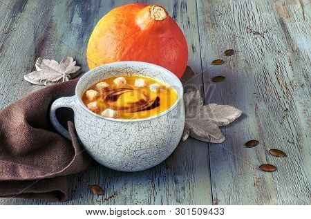 Pumpkin Soup  Served In Blue Ceramic Cup With Croutons And Pumpkin Oil On Light Blue Rustic Table, T