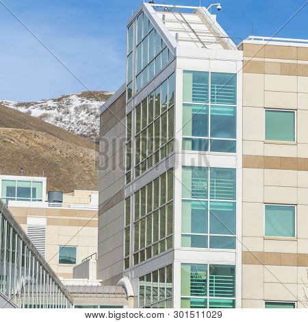 Square Sunny Day View Of A Modern Building Exterior With A Glass Walled Skybridge