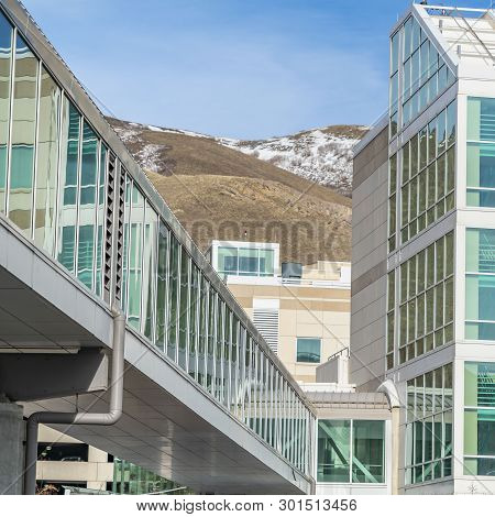 Clear Square Sunny Day View Of A Modern Building Exterior With A Glass Walled Skybridge