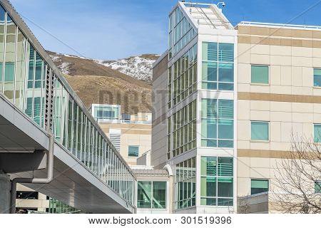 Sunny Day View Of A Modern Building Exterior With A Glass Walled Skybridge