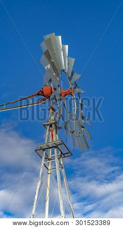 Clear Vertical Close Up Of A Windpump With Vibrant Blue Sky And Puffy Clouds In The Background