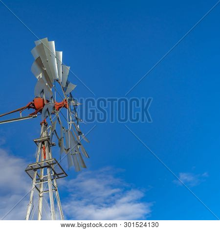 Clear Square Close Up Of A Windpump With Vibrant Blue Sky And Puffy Clouds In The Background