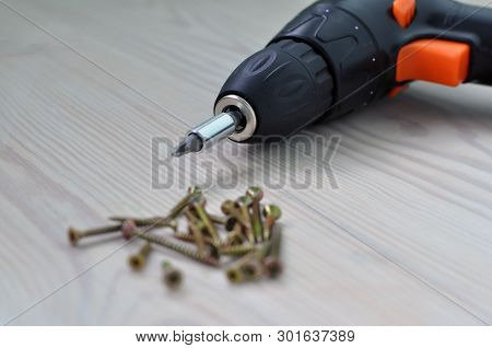 Electric Screwdriver And Screws On A Wooden Table.