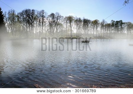 The Boat Floats On The River Through The Fog Early In The Morning With Two People.