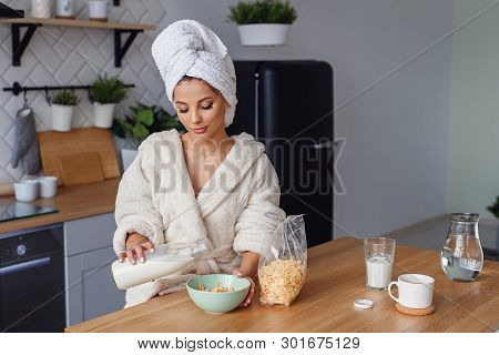 Close Up Young Woman In Bathrobe Pours Milk In Dep Plate With Corn Flakes. Pretty Girl Has A Healthy