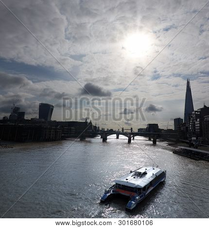 Sun Shining Through The Clouds On Skyscrapers Of London City Over River Thames With Passenger Boat O