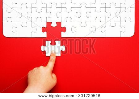 Childrens Hand Moves A Piece Of White Puzzle On A Red Background