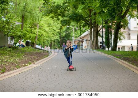 Little Boy Riding Scooter In City Park In Aummer. Kids Sports Outdoors. Happy Child Playing With His